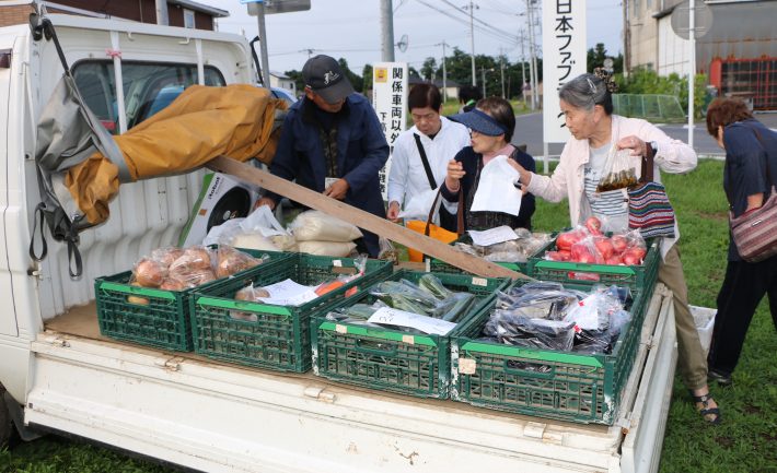 トラックに並べられた野菜を品定めする女性たち