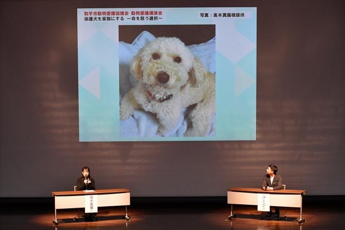 高木真備氏とユージ氏がパネルディスカッションをしている。スクリーンに高木真備氏の飼い犬の写真が投影されている。