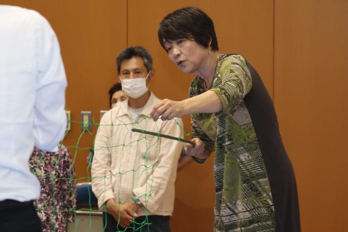 講師の石川先生がネットと支柱を手に取り、ゴーヤを育てるかた法を実演によって参加者に教えている。