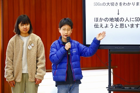 取手西小学校の代表生徒がプレゼンテーションで発表スライドを指さしながら説明を行っている。