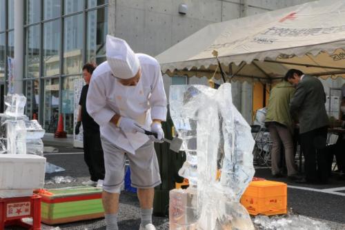 魚らしき形の氷彫刻を作成している男性。のみのような道具を手にしている