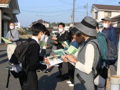 学生らしき人が並んでいる人にプリントの入った封筒を渡している写真