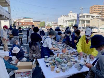 陶器を机に並べる人とそれを買おうと列をなして選んでいるの写真。