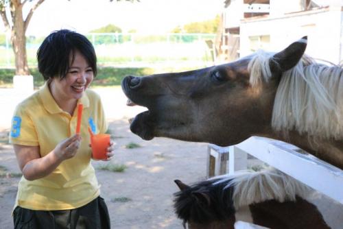 ponyの頭をなでる若い女性の写真。ニンジンをあげようとしている