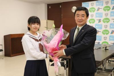 スーツ姿の男性が制服姿の中学生女子に花束を渡して笑顔を向けている