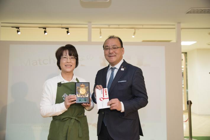 優秀賞授与の様子。賞の封筒を手にした龍ケ崎市長とたてを手にした天ヶ谷桂子さんが並んで記念撮影。