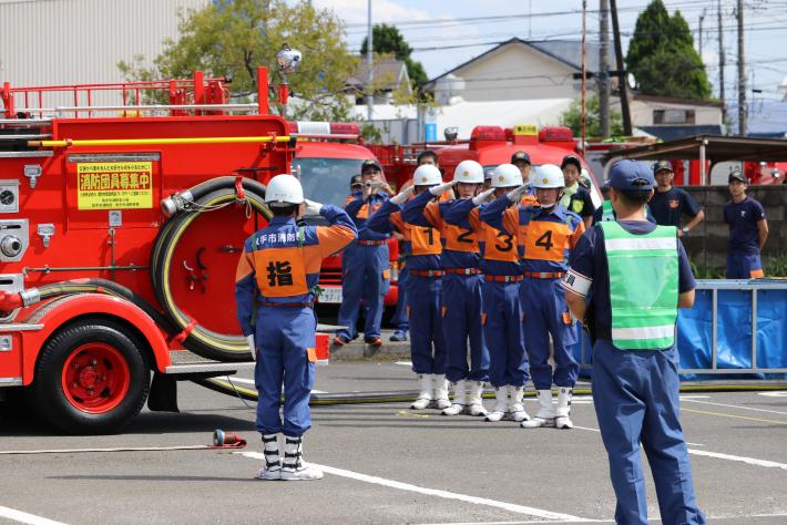 消防車の横で団員が並んで敬礼をし、競技の終了報告を行っている様子