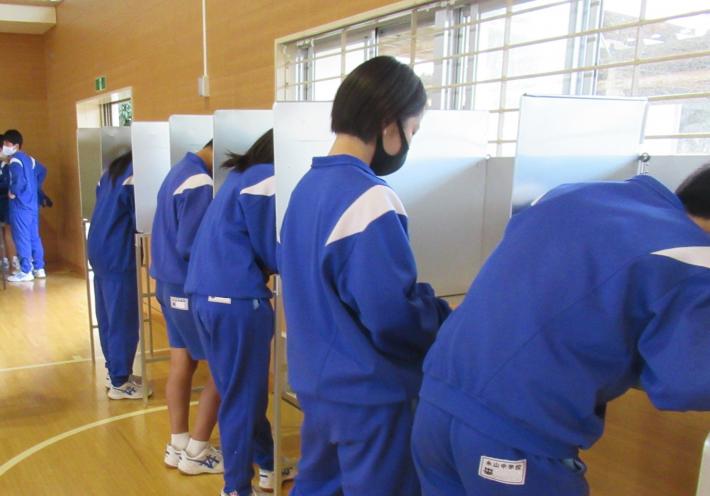 永山中学校の生徒会選挙で2人用の記載台を使用し、投票用紙に記入している様子