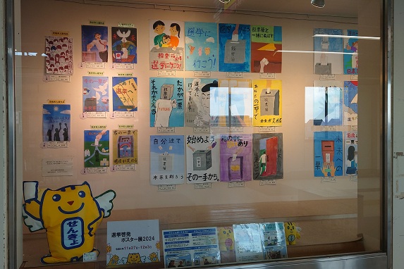 藤代駅市民ギャラリーの様子。応募作品がガラス張りのギャラリー内に貼られている。手前には「めいすいくん」のぬいぐるみ等が置かれる。