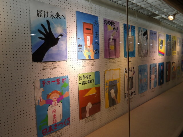 取手駅市民ギャラリーでのポスター展の写真。ガラス張りのギャラリー内にポスターが縦に2枚、横に10列以上並んでいる。