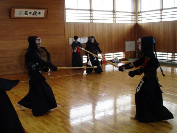 藤代剣道クラブ員が剣道の試合をしています。武道場内で面をつけて試合をする生徒とそれを観戦する生徒たち。