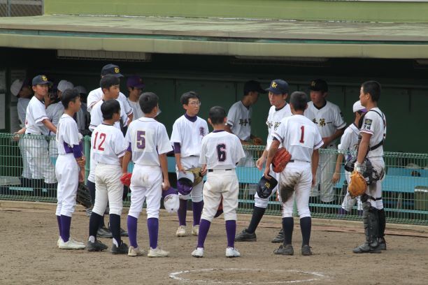 野球円陣。グラウンドのベンチの前で、輪になって何かを話している様子の選手達。