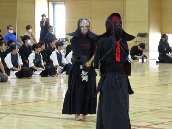 剣道新人戦試合の様子。戦う2人の背景に応援中らしいほかの生徒たちが座っているようすが見える。