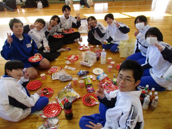 お楽しみのクリスマス会の様子。お菓子を前に、輪になって座り、カメラに向かってポーズをとる中学生たちの様子。