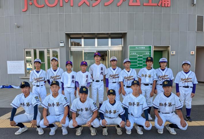 スタジアム入り口の前で、ユニフォーム姿で2列に整列して並んで記念撮影をしている野球チームの様子。