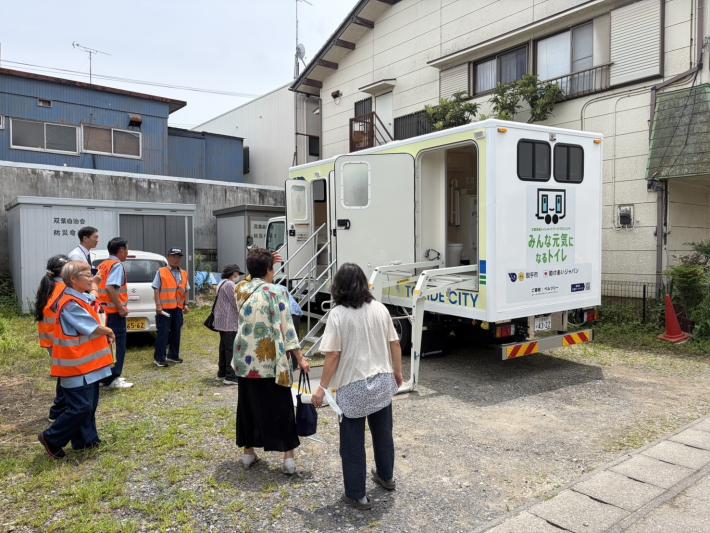 双葉自治会館前にトイレトラックを展示し、複数のかたに見学いただいている写真
