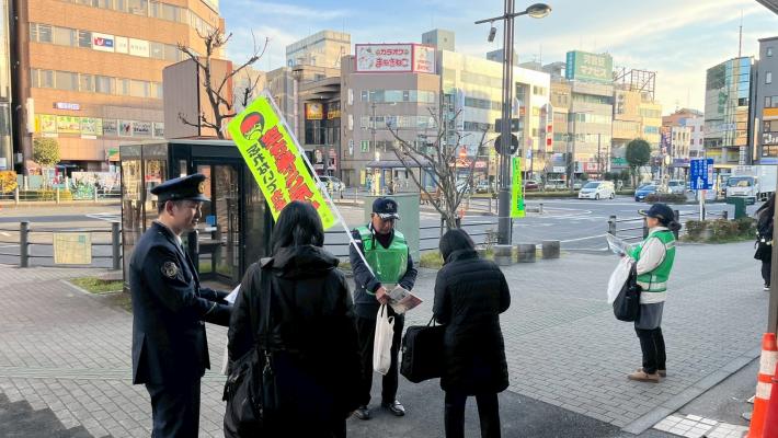 防犯連絡員や警察官が市民に防犯対策の徹底を呼びかけながら啓発品を配布する様子