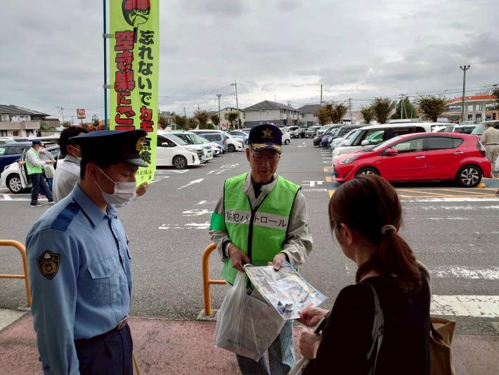 防犯連絡員と警察官が来店客に啓発品を配布する様子