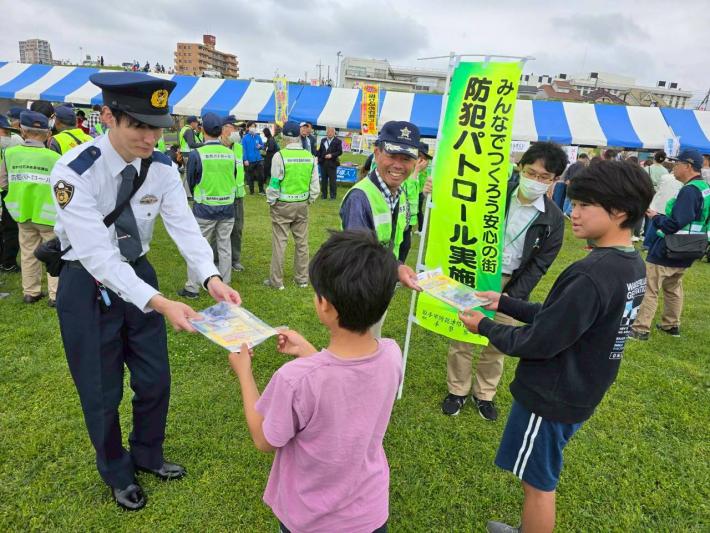防犯連絡員と取手警察署員が来場した子どもへ啓発品を配布している様子