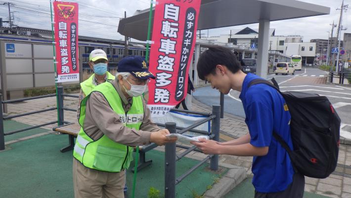 藤代駅北口自転車駐車場で、防犯連絡員が駐車場利用者に啓発品を配布している様子。