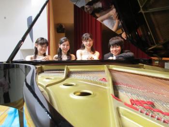 舞台上で4名のピアノ演奏者がピアノの前で集合している写真。