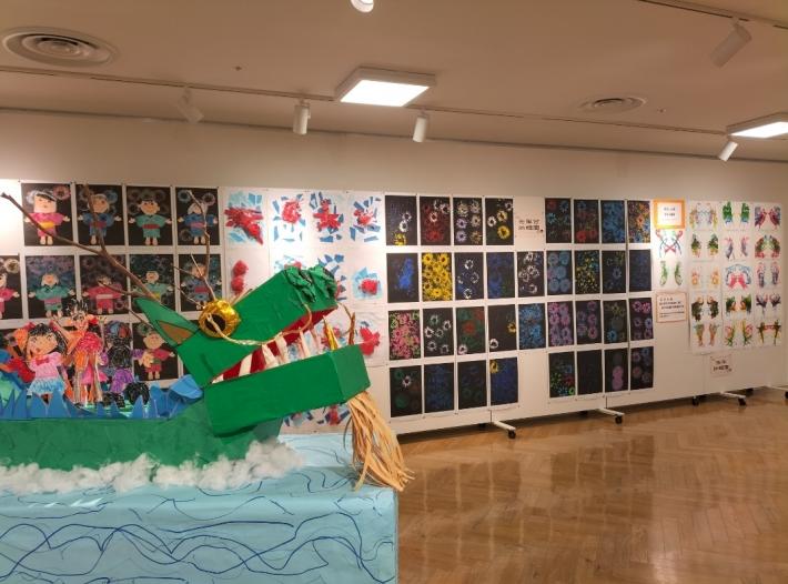 画像手前に緑の辰の立体作品があり、奥の壁に浴衣を着た子どもたちの絵画作品がある様子