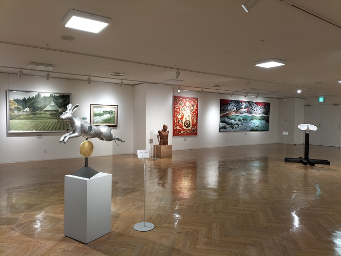 床に3点の彫刻作品、奥の壁に4点の平面作品が展示されている様子