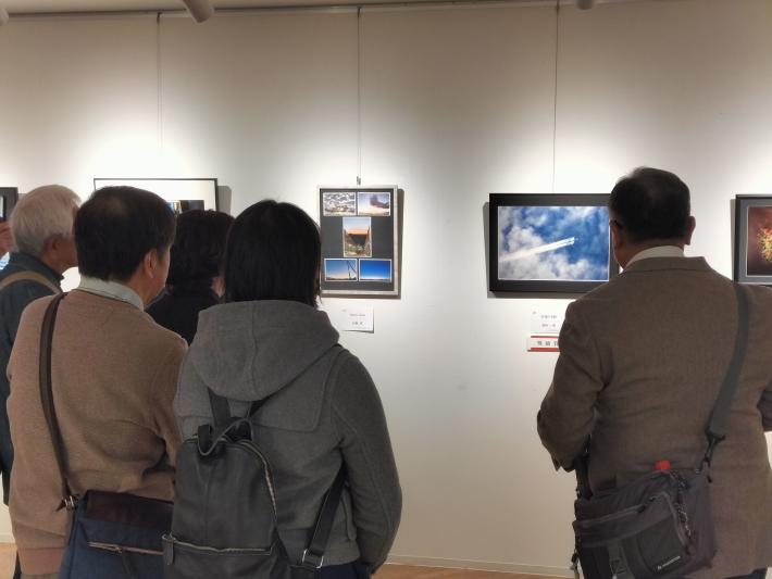 人々が壁に飾られた写真作品の前で話している第2部合評会の様子