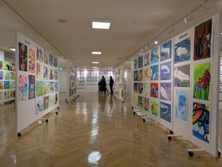 両側のパネルと奥の壁一面に数多くの作品が飾られている第3部会場の様子