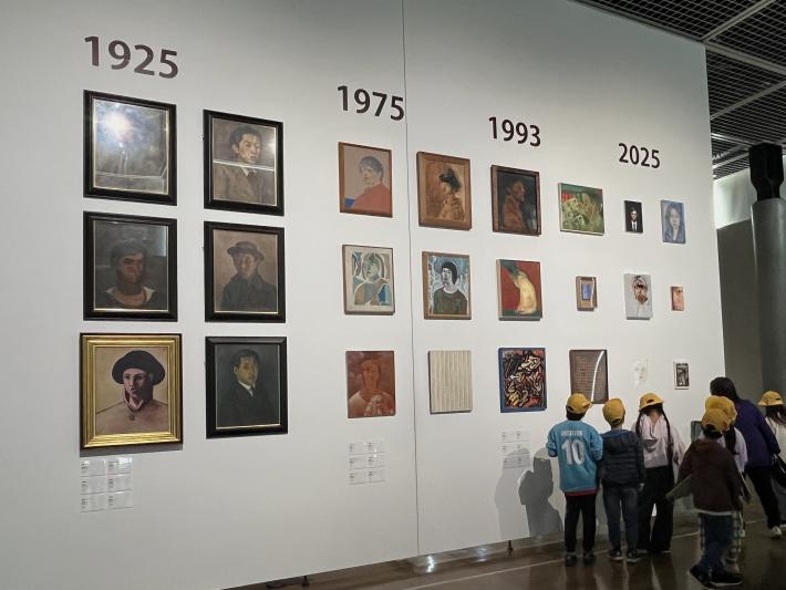 小学生5人が自画像の展示の前で鑑賞している様子