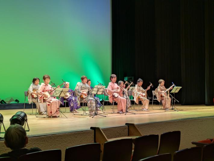 市民会館の舞台で、日々の練習の成果を披露する三味線奏者たち。彼女たちが紡ぎ出す音色は、日本の伝統文化への愛情を感じさせます。
