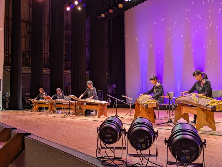 5人の熟練した女性琴奏者たちが椅子に座りながら、息の合った演奏で観客を魅了しています