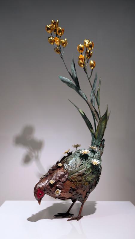 尾を上げて下を向いているヤマドリの立体作品。ヤマドリの体は複数の植物で構成され、尾から金の花、体毛から白い花が飛び出ている。