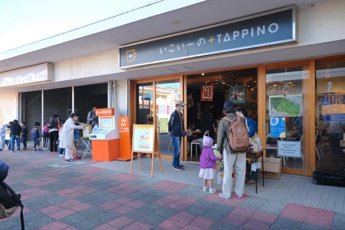 いこいーの＋TAPPINOの看板がついた建物の入り口に人がいる様子