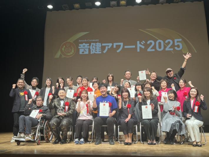 壇上で受賞者と審査員併せて約20名が手を上げて記念撮影している様子