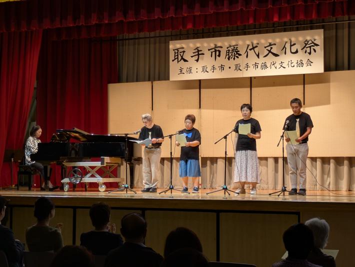 音楽祭で、壇上に立つ4人の男女が、ピアノの伴奏に合わせて真剣な表情で歌を披露しています