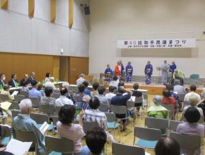着物姿の男女数人が大勢の観客を前に舞台に立っている様子