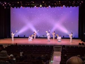 市民会館の舞台で、7人の女性が優雅に日本舞踊を舞っている様子