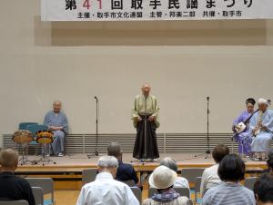 着物姿の男性が舞台で唄っている様子