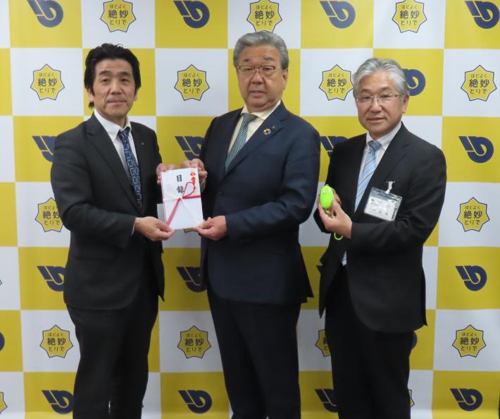 「ほどよく絶妙とりで」バックパネルの前で、防犯ブザー、目録を手に写真に写る支店長、市長、教育長