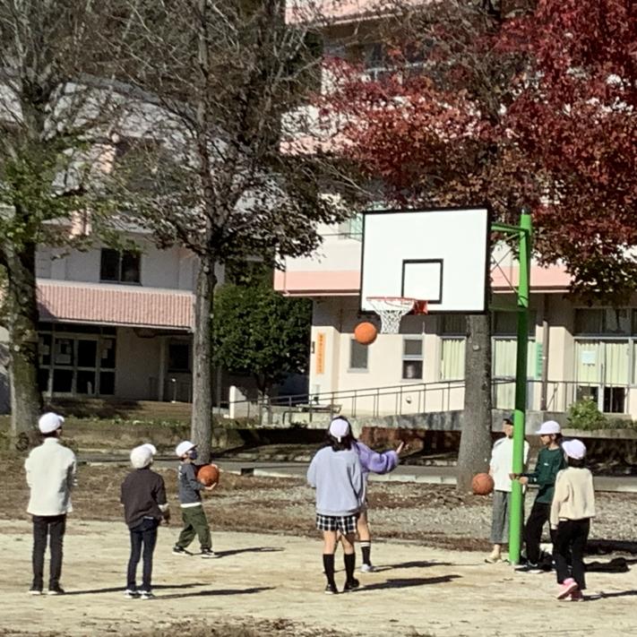 8人の児童がバスケットゴールで遊んでいる。ボールがゴール付近にある。