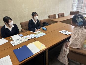 女子高生2名と着物を着た女性が机を挟んで話をしている