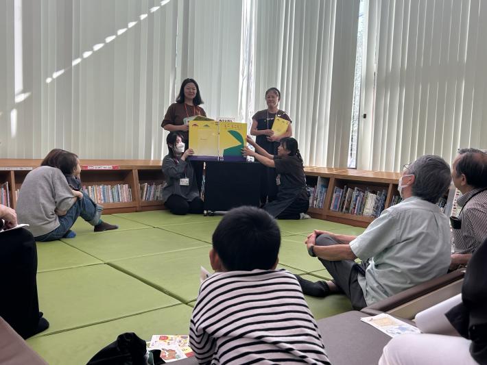 床に座って絵本の読み聞かせを聞く人たち