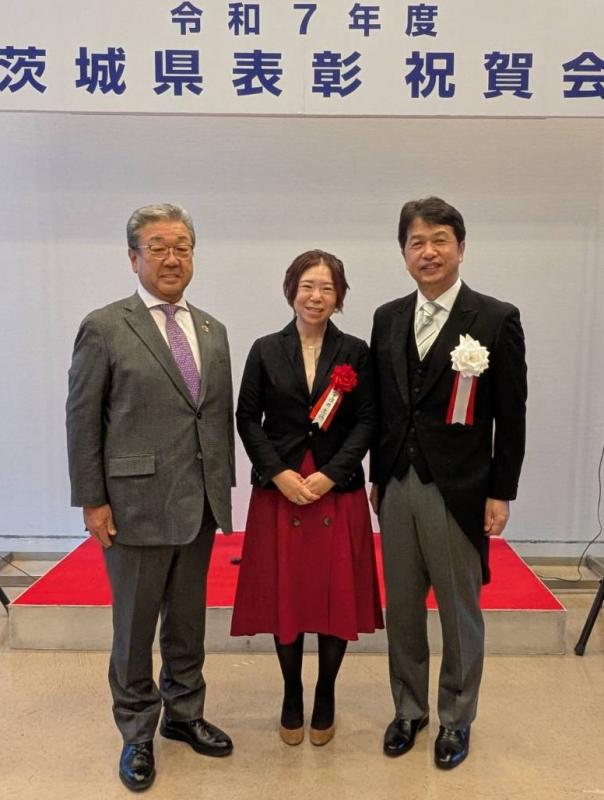 祝賀会ひな壇の前での正装の男性とスーツ姿の女性と男性のスリーショット