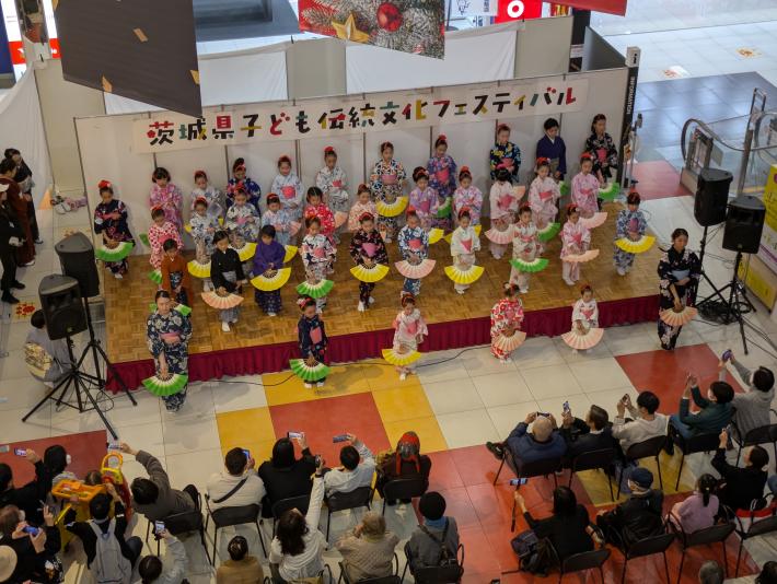 特設舞台に大勢の着物姿の子供が舞踊の扇子を持って客席に向かっている