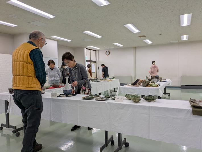 テーブルにたくさんの陶芸作品が飾られ数人の人が見ている様子