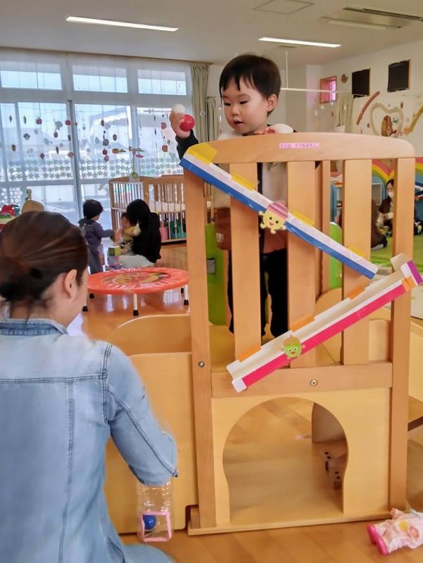 滑り台の上からボールを転がしている男の子とお母さんがいる写真