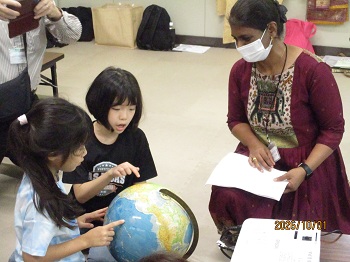 インドの民族衣装を着た女性と小学生二人が地球儀を見ている写真