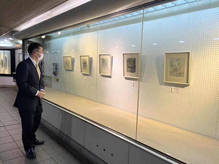 ガラスのショーケース越しに絵画を見る男性