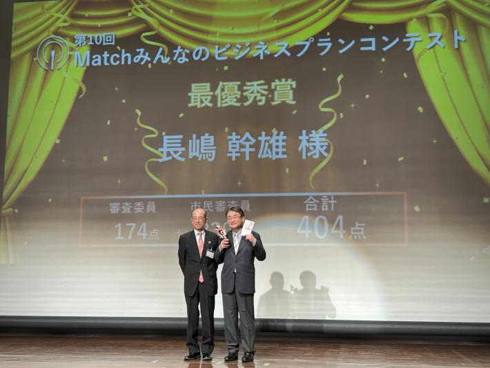 最優秀賞の楯を手に持つ男性とその隣に立つ男性